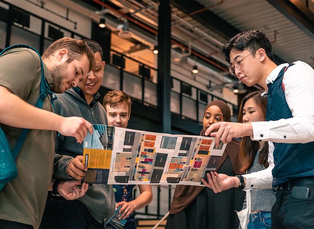 Six students are standing and gathered around a leaflet together